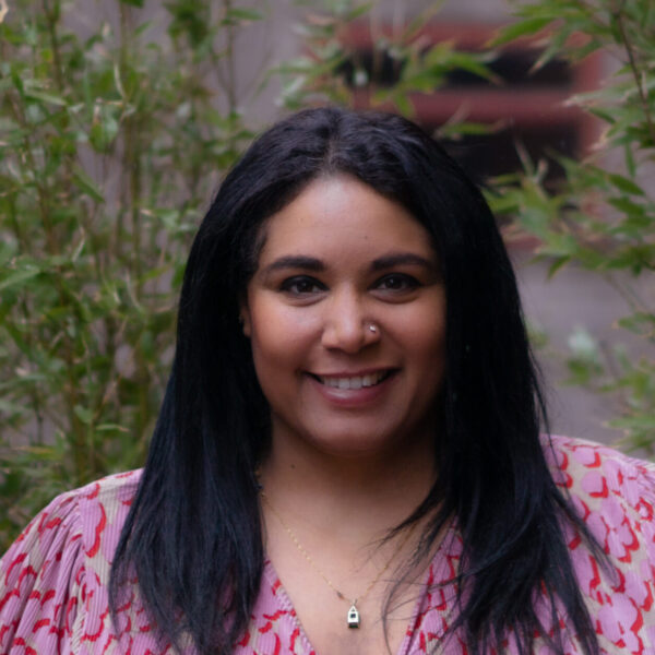A cheerful woman with long black hair dressed in a pink shirt, radiating positivity.