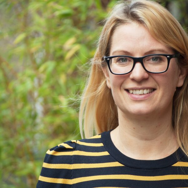 A cheerful woman in a striped shirt and glasses, showcasing a warm smile that brightens the scene.