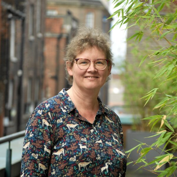 A woman with glasses stands on a balcony, enjoying the view and the fresh air.