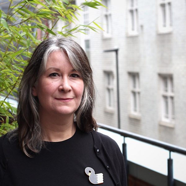 A woman with gray hair poses in front of a contemporary building, exuding grace and strength in her stance.